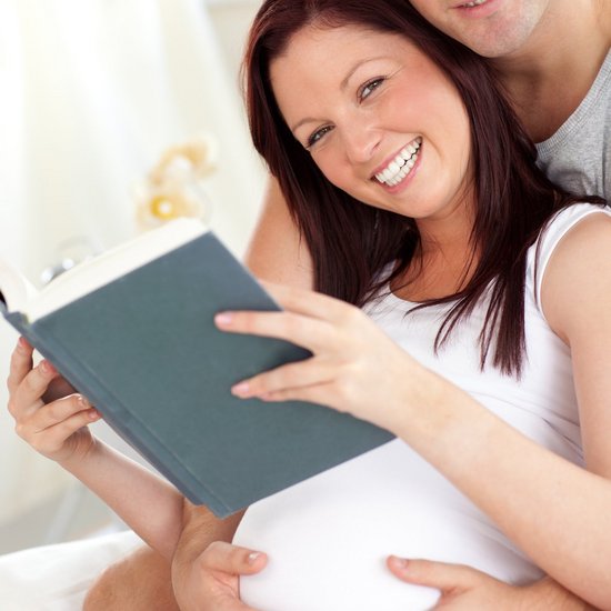 Glückliche zukünftige Eltern sitzen und lesen ein Buch.