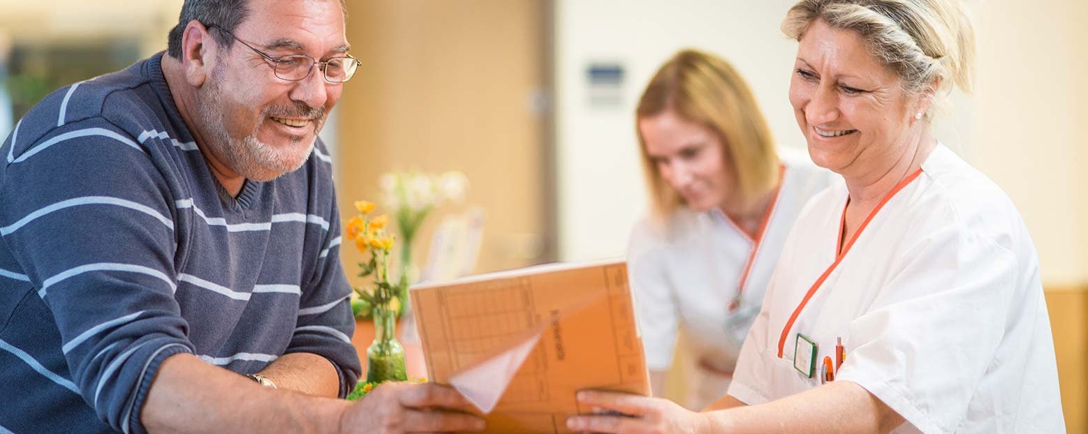 Ein Patient und eine Krankenschwester stehen an einem Tresen und schauen gemeinsam eine Patientenakte an