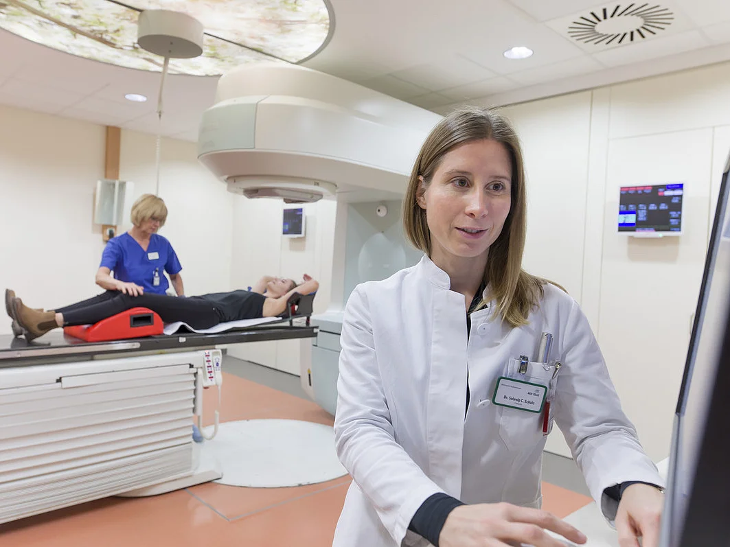 Ärztin bedient ein Gerät während ein Patient zur Strahlentherapie vorbereitet wird.
