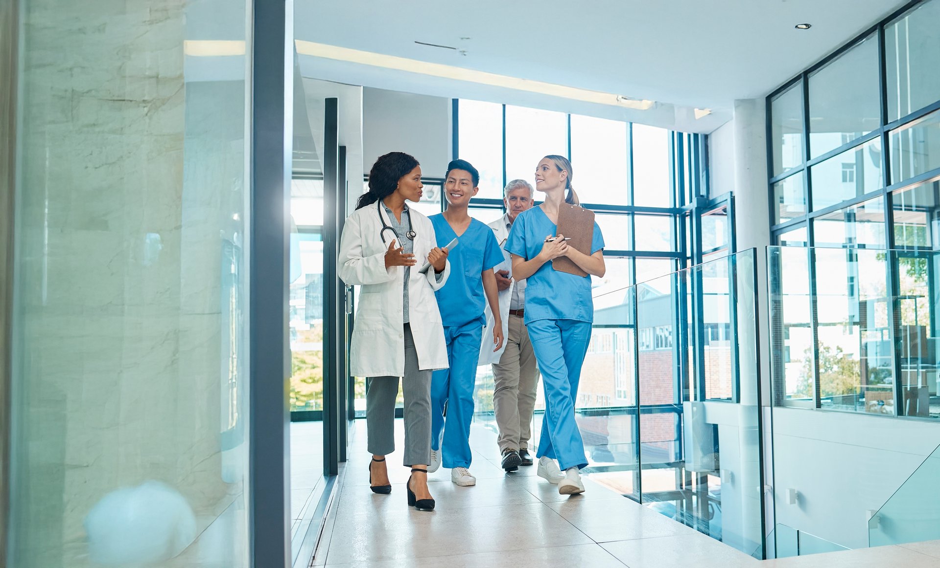 Ein Team aus medizinischem Fachpersonal geht gemeinsam durch einen modernen Klinikflur – sie unterhalten sich und wirken engagiert.